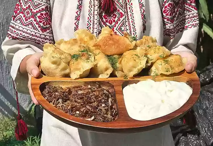 Ukrainian woman holds a plate of vareniki (dumplings) with fried onions and sour cream.